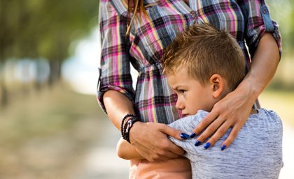 A small boy clings to his carer